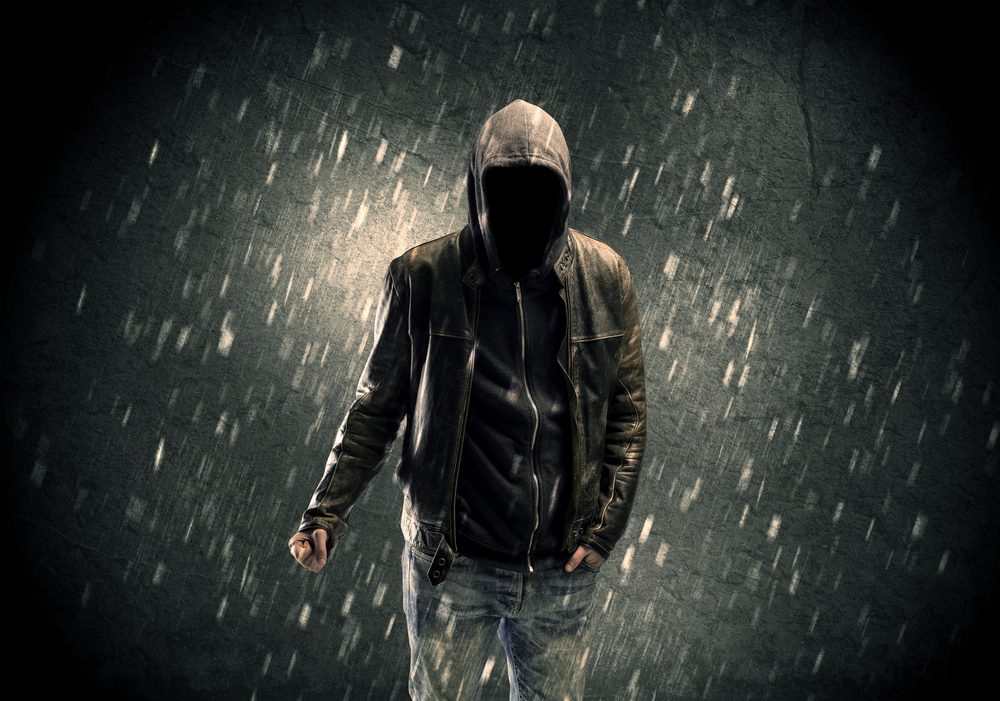 A faceless misterious man in hoodie and leather jacket standing in the dark with a visible silhouette concept